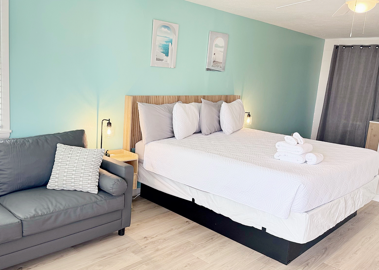 Bedroom with bed, sofa, and light blue wall. Towels on the bed and artwork above.