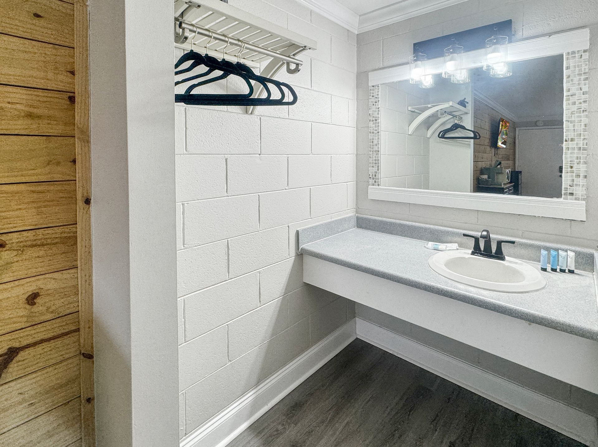 Bathroom with a white countertop, sink, and mirror, with gray-tiled flooring and a light wood wall on the left.