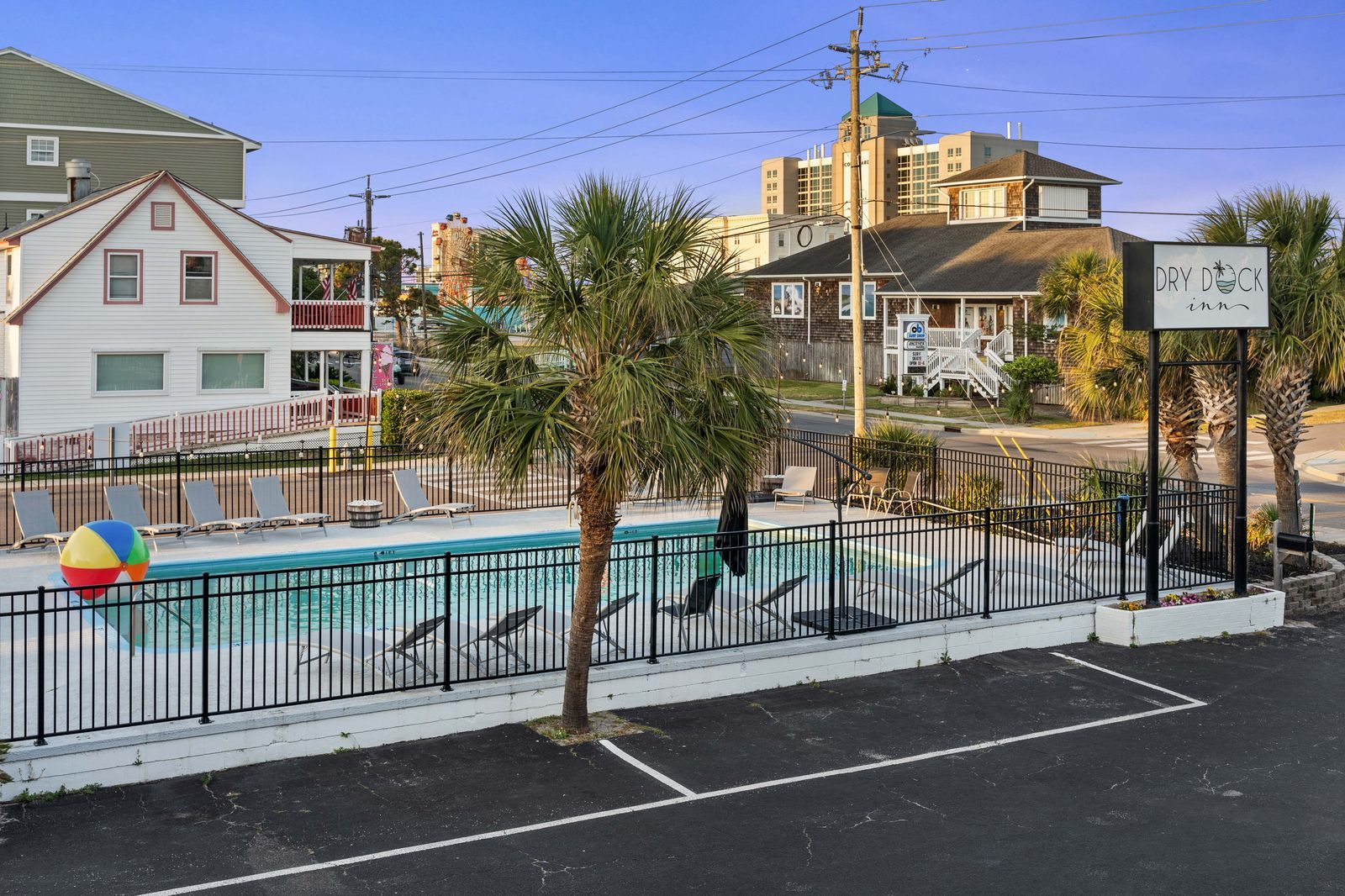 A motel pool area with a fence, parking, and buildings, including a sign that says 