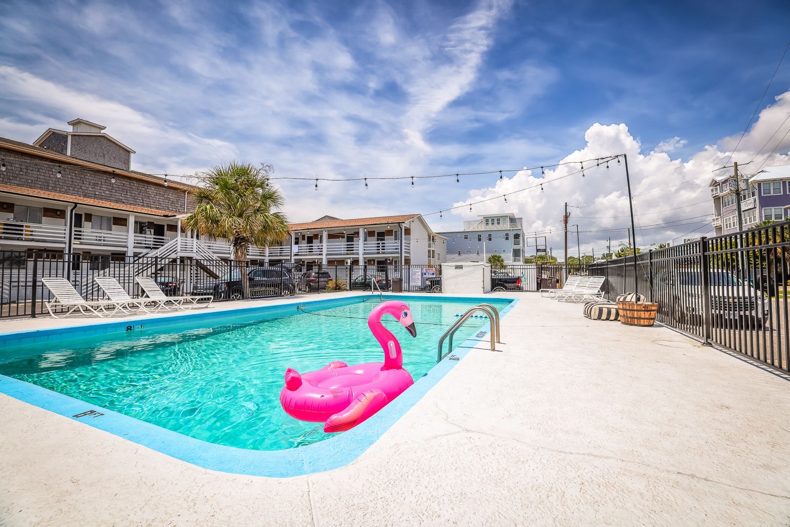 A swimming pool with a pink flamingo float under a partly cloudy blue sky.