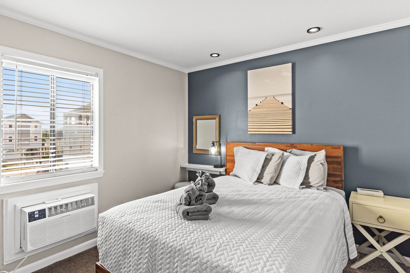 Bedroom with a queen-sized bed, blue accent wall, window, and an air conditioner.