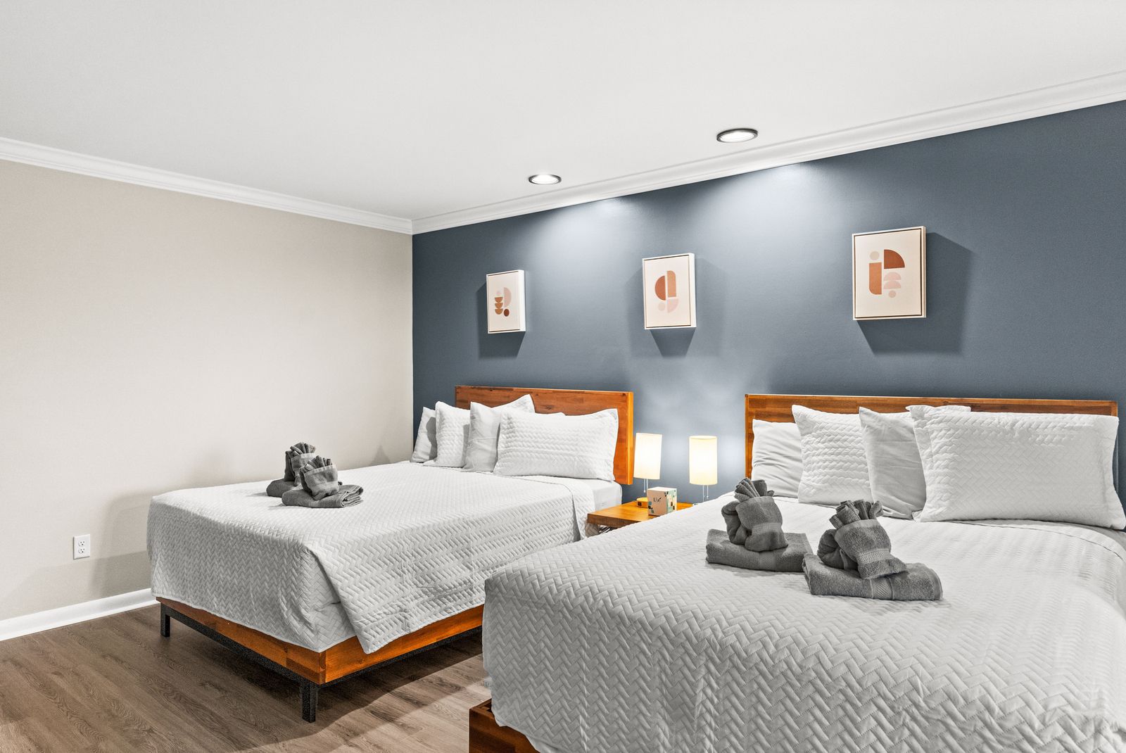 Two beds in a room, white bedding, blue accent wall with art, wood floors.