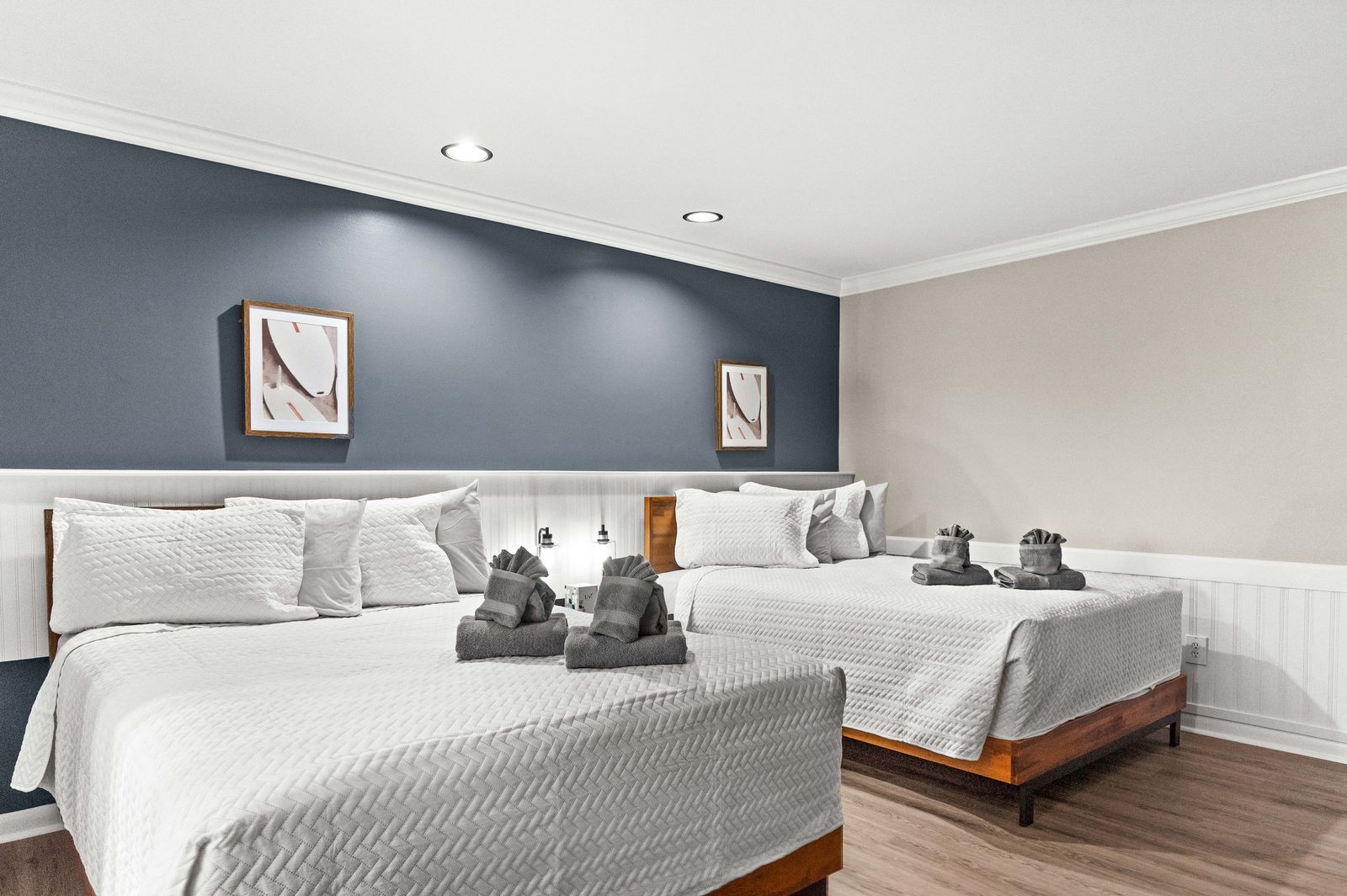 Two queen beds in a room, gray walls, white bedding, framed art, and folded towels.