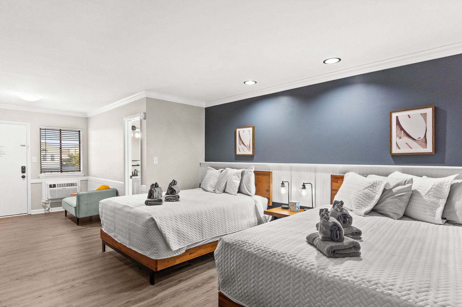 Hotel room with two queen beds, blue accent wall, and sitting area.