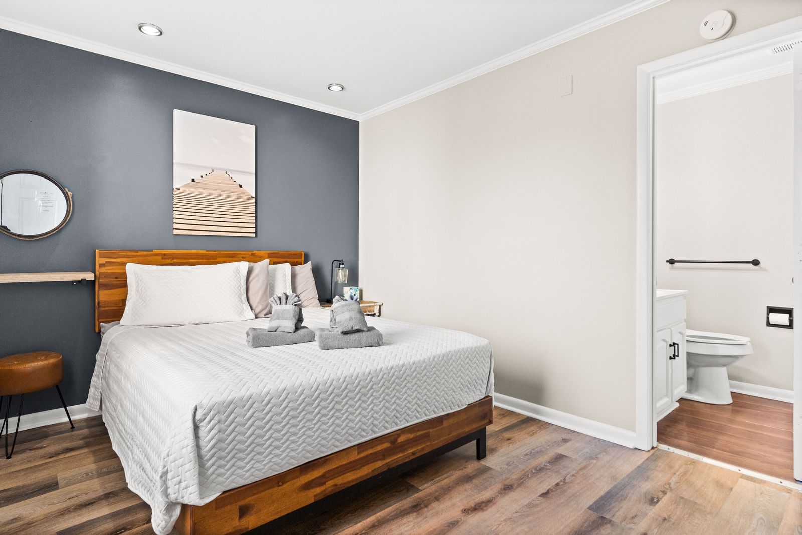 Bedroom with a wooden bed frame, grey wall, and a doorway leading to a bathroom. The room has wood flooring.