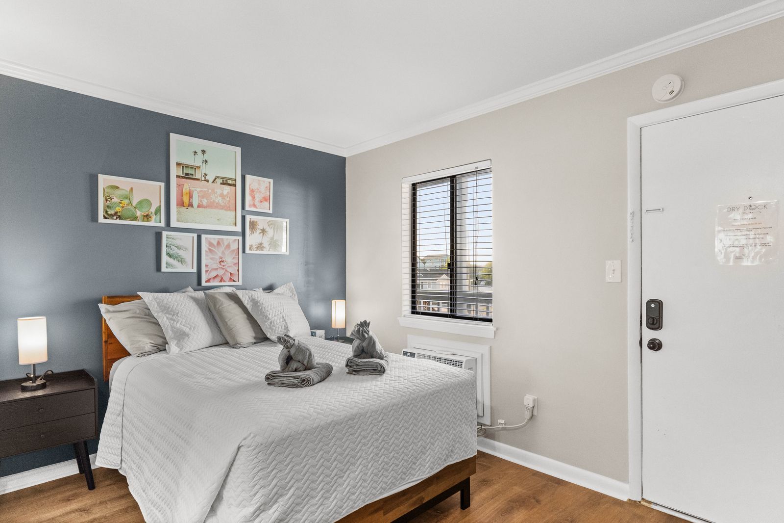 Bedroom with a bed, artwork, a window, and a closed white door.