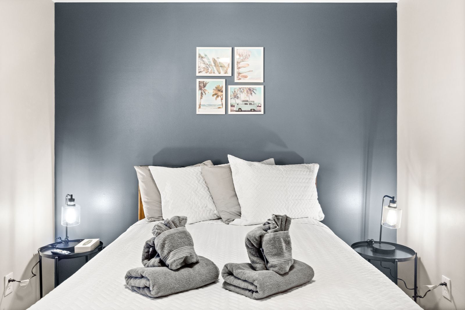 Bedroom with blue wall, white bedding, two bedside lamps, and small art.