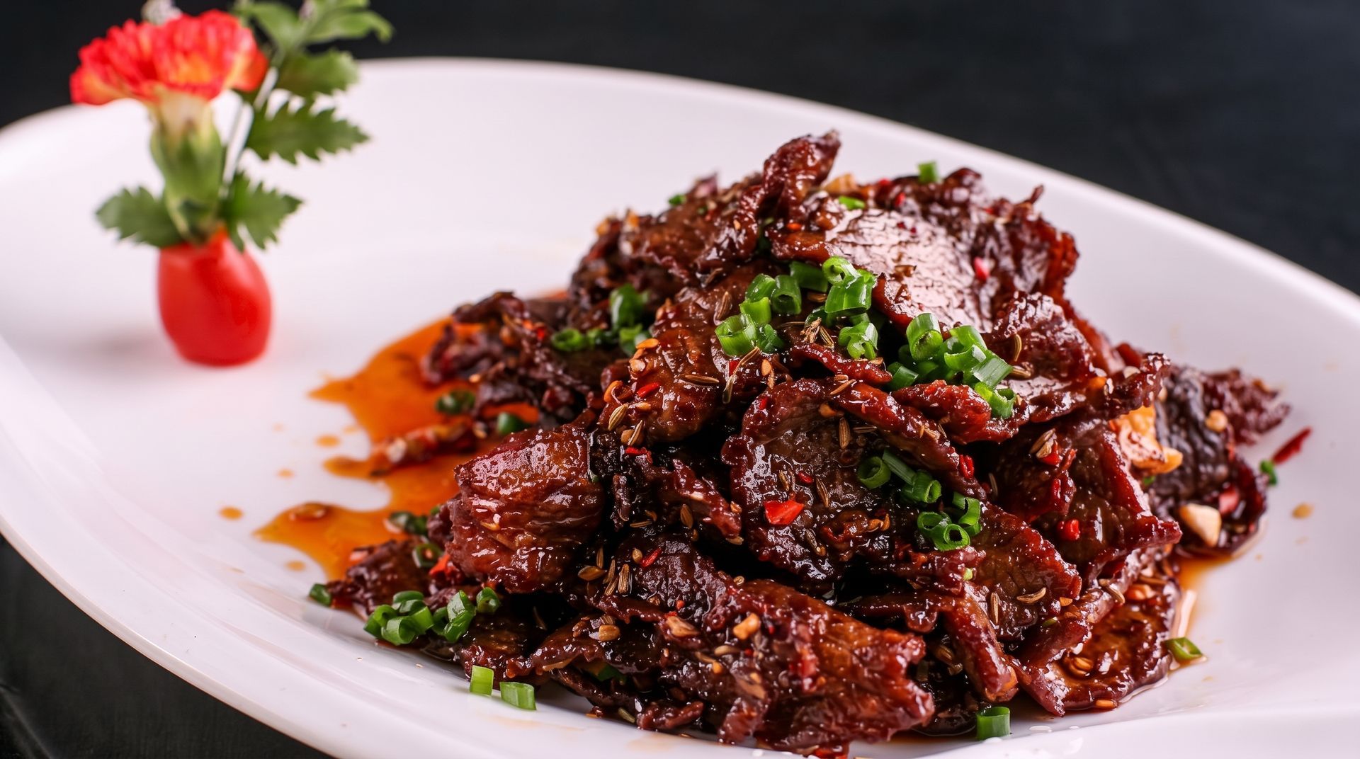 Dark glazed meat stir-fry garnished with herbs, plated on a white dish with a strawberry garnish