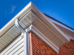 The corner of a brick house with white siding and gutters