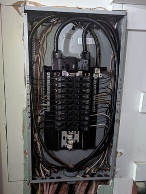 Open electrical breaker panel with wires and circuit breakers inside a wall cabinet