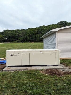 Outdoor beige generator unit beside a house on a concrete pad, with grassy yard and trees behind.