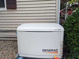 White Generac generator beside a house with beige siding and gravel ground