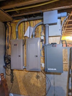 Electrical panels and wiring mounted on a basement wall under exposed beams.