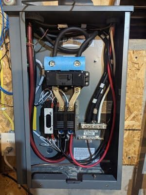 Open electrical panel with blue breaker and red/black wiring inside a gray metal cabinet