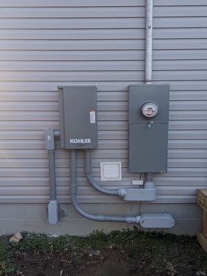 Gray utility boxes and gas meter mounted on a house exterior wall with conduit and piping.