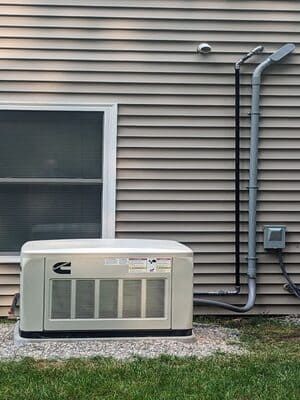 Outdoor generator beside a house with beige siding, near a window, utility boxes, and gravel