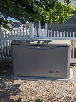 Gray Kohler generator outdoors beside a white picket fence and a tree