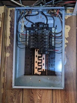 Open electrical breaker panel with exposed wiring and circuit breakers in a wall recess.
