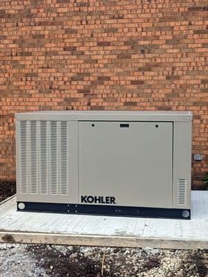 Kohler generator unit on a concrete pad against a brick wall