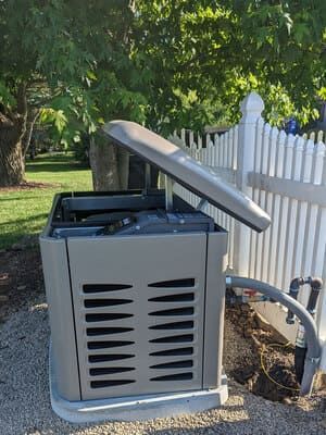 Outdoor HVAC unit beside a white fence, with the top panel propped open under trees.