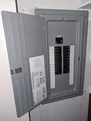 Open electrical breaker panel on a tiled wall with the cover door ajar.