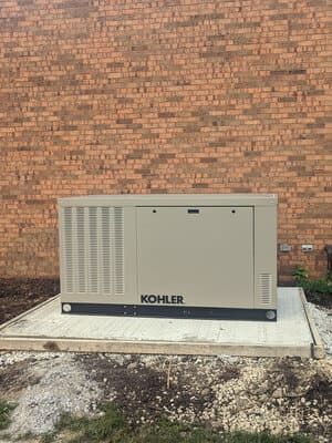 Kohler generator on a concrete pad against a brick wall outdoors
