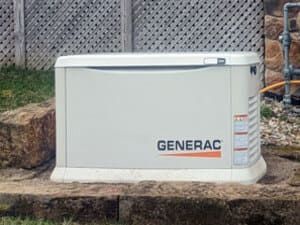 White Generac home standby generator on a concrete pad beside a house wall and fence.