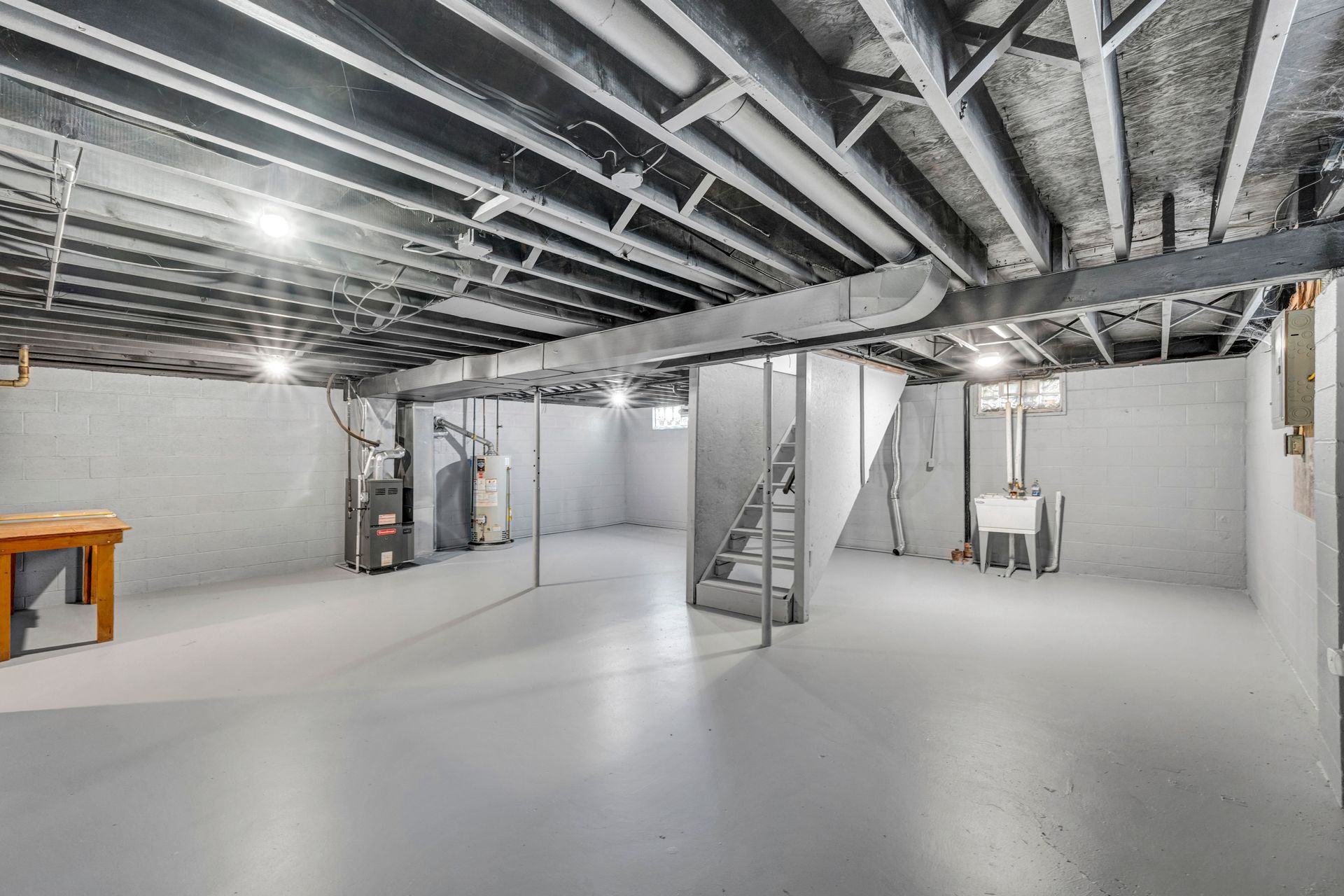 Empty basement with exposed ceiling joists, white walls, concrete floor, and a staircase under construction