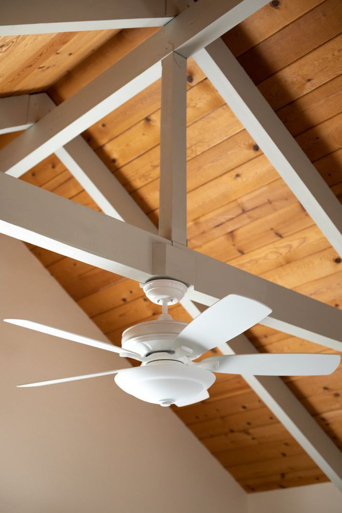 Ceiling fan with white blades on a wood-paneled vaulted ceiling with white beams