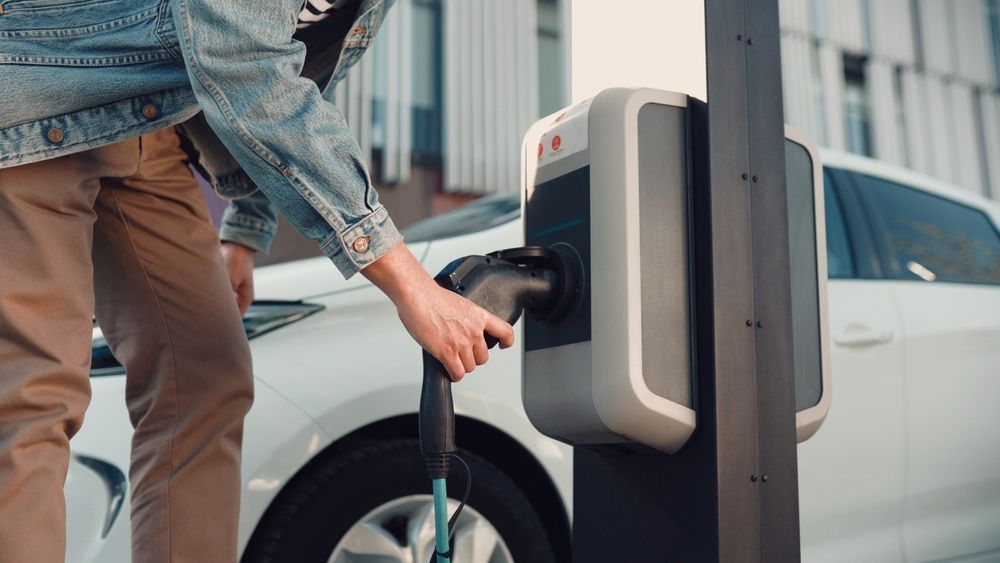 Person plugs an EV charging cable into a white car at a station