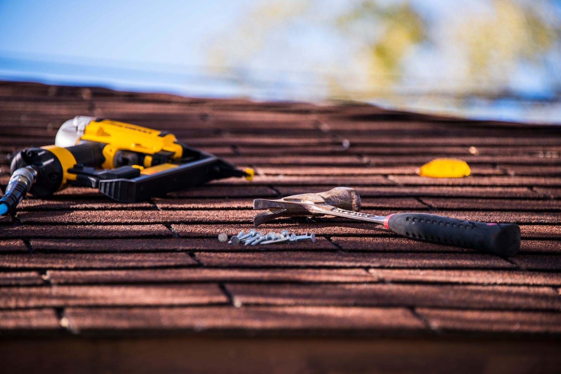Hammer, nails, and a nail gun lying on a shingled roof.