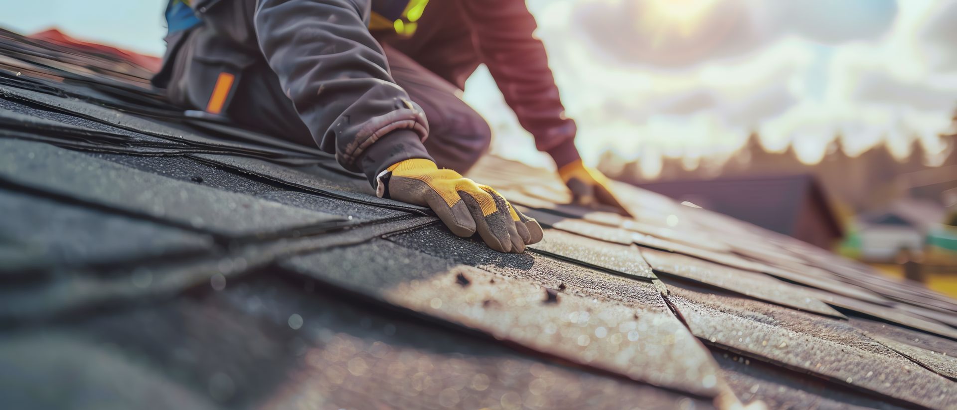 Worker installing or repairing roof shingles while wearing protective gloves. 