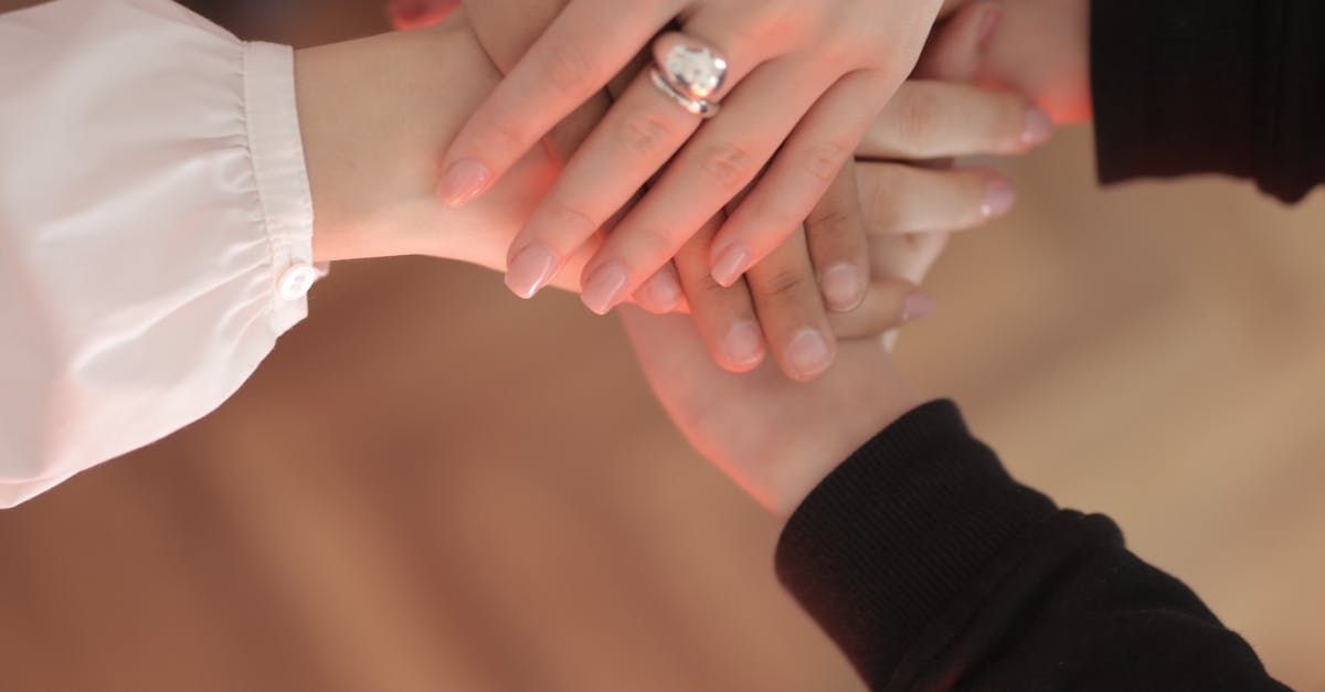 Hands stacked on top of each other; a woman wearing a ring with a silver flower design; white and black sleeves.