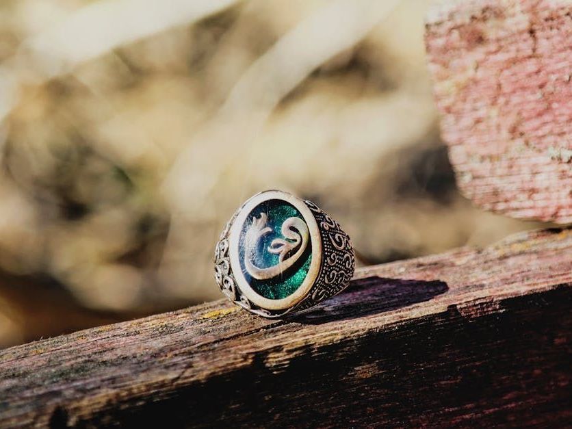 Silver ring with Arabic calligraphy set on a green stone, resting on weathered wood.