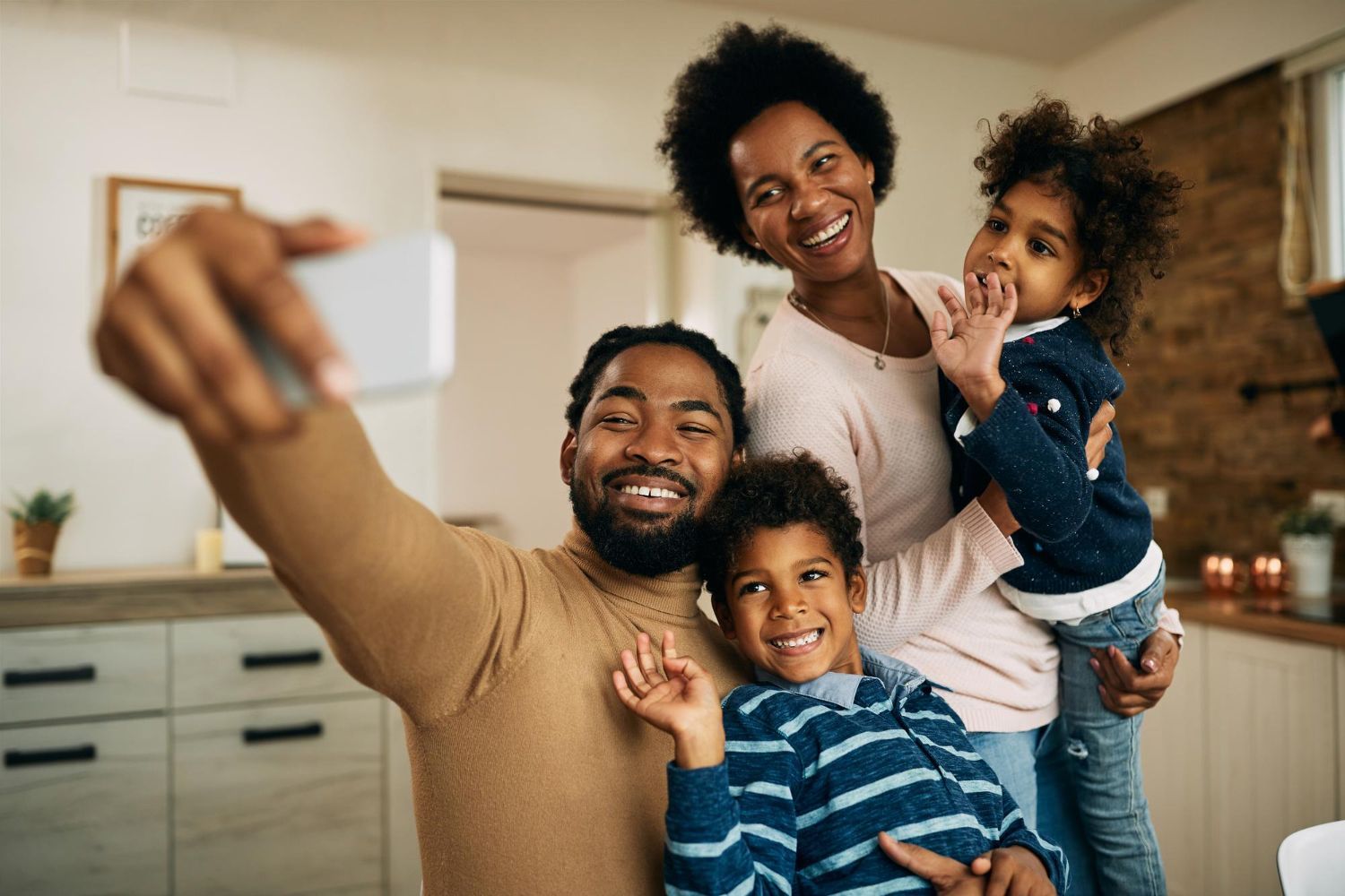 Family taking a selfie together in a cozy kitchen, smiling with two children close by