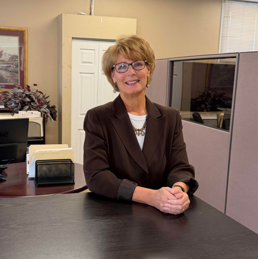 Cathy Moran in glasses stands behind a reception counter in an office cubicle.