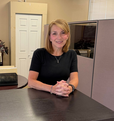 Lauren Hobin seated at a desk in an office, smiling with hands clasped.