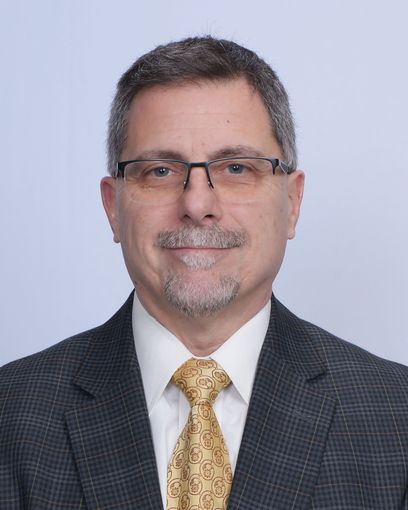 Scott Grande in glasses, suit jacket, and gold tie on a light background