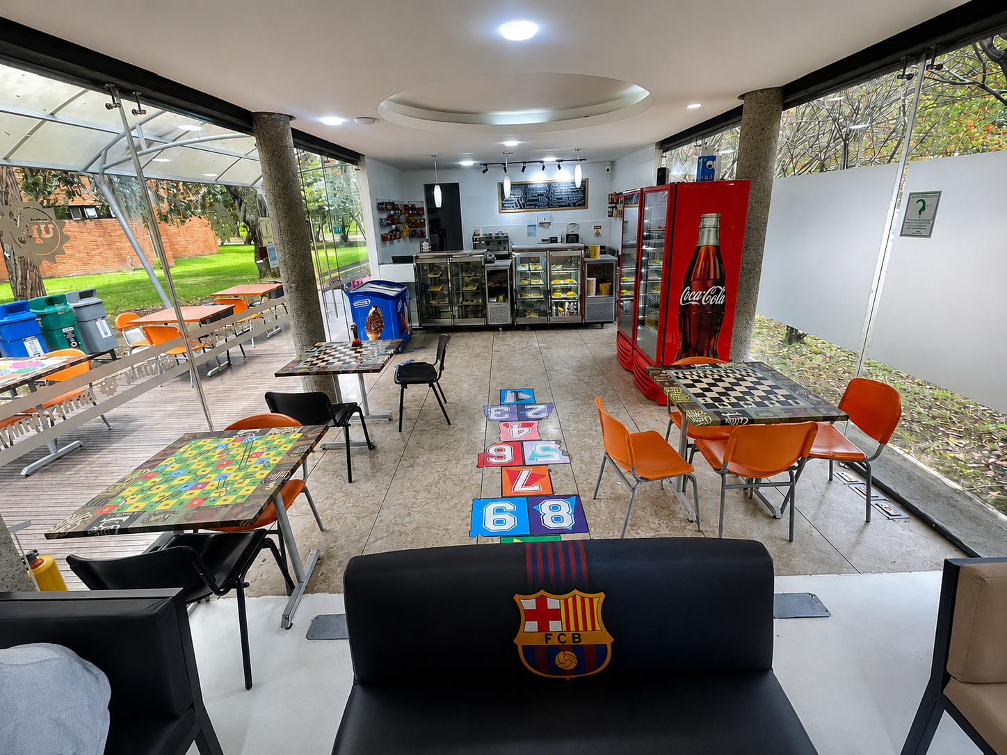 Patio exterior con mesas, sillas y una máquina expendedora roja bajo un techo cubierto.
