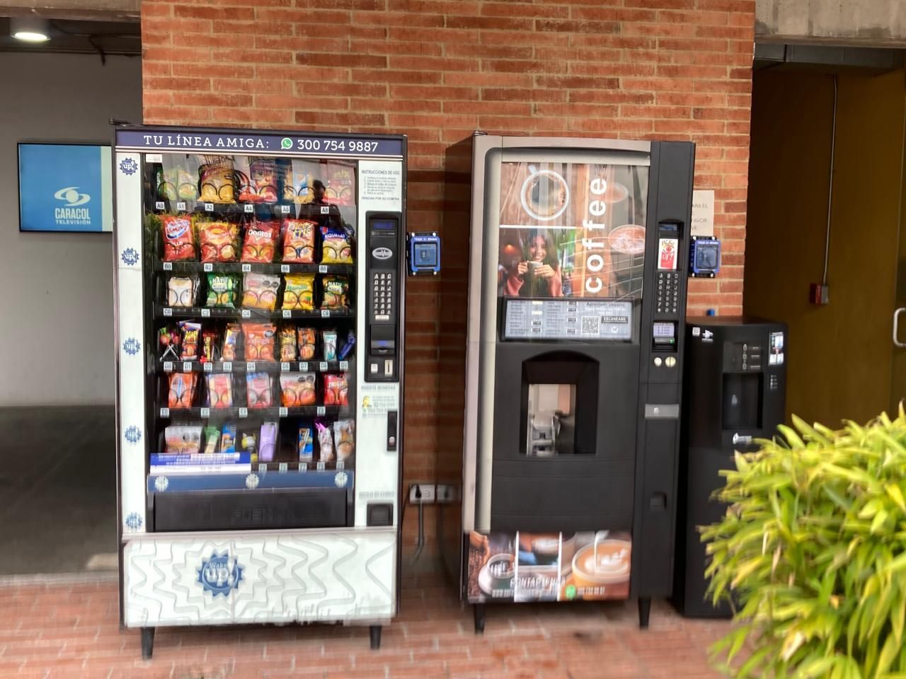 Máquinas expendedoras de aperitivos y bebidas contra una pared de ladrillos en un pasillo.