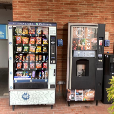 Dos máquinas expendedoras contra una pared de ladrillos, una con aperitivos y otra con café.