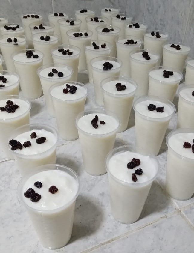 Hileras de copas blancas de postre cubiertas con frutos rojos oscuros sobre una encimera, preparadas para servir.