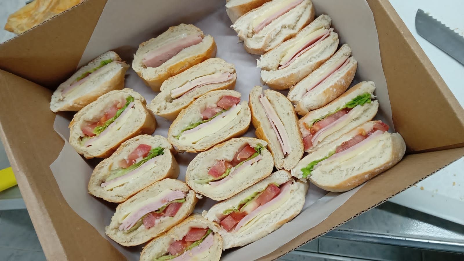 Caja de bocadillos variados cortados en tiras, dispuestos en filas sobre papel pergamino.
