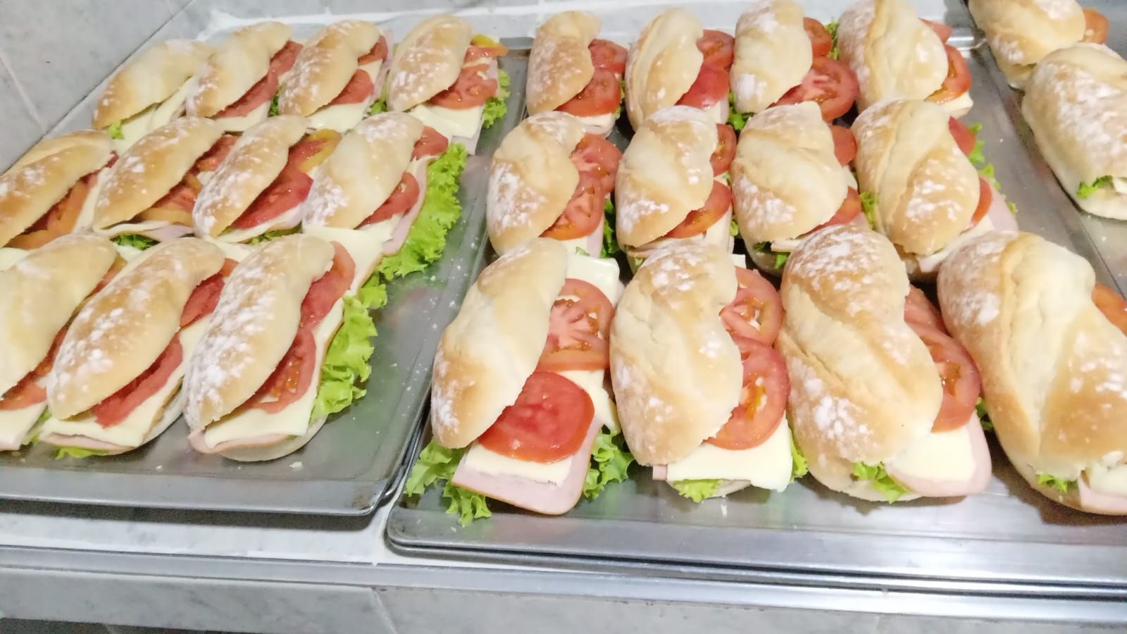 Bandejas de bocadillos de baguette con salmón y lechuga expuestas en el mostrador de una charcutería.