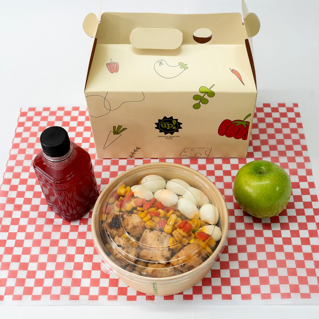 Comida en una fiambrera con tapa transparente, botella de agua roja y manzana verde sobre un mantel