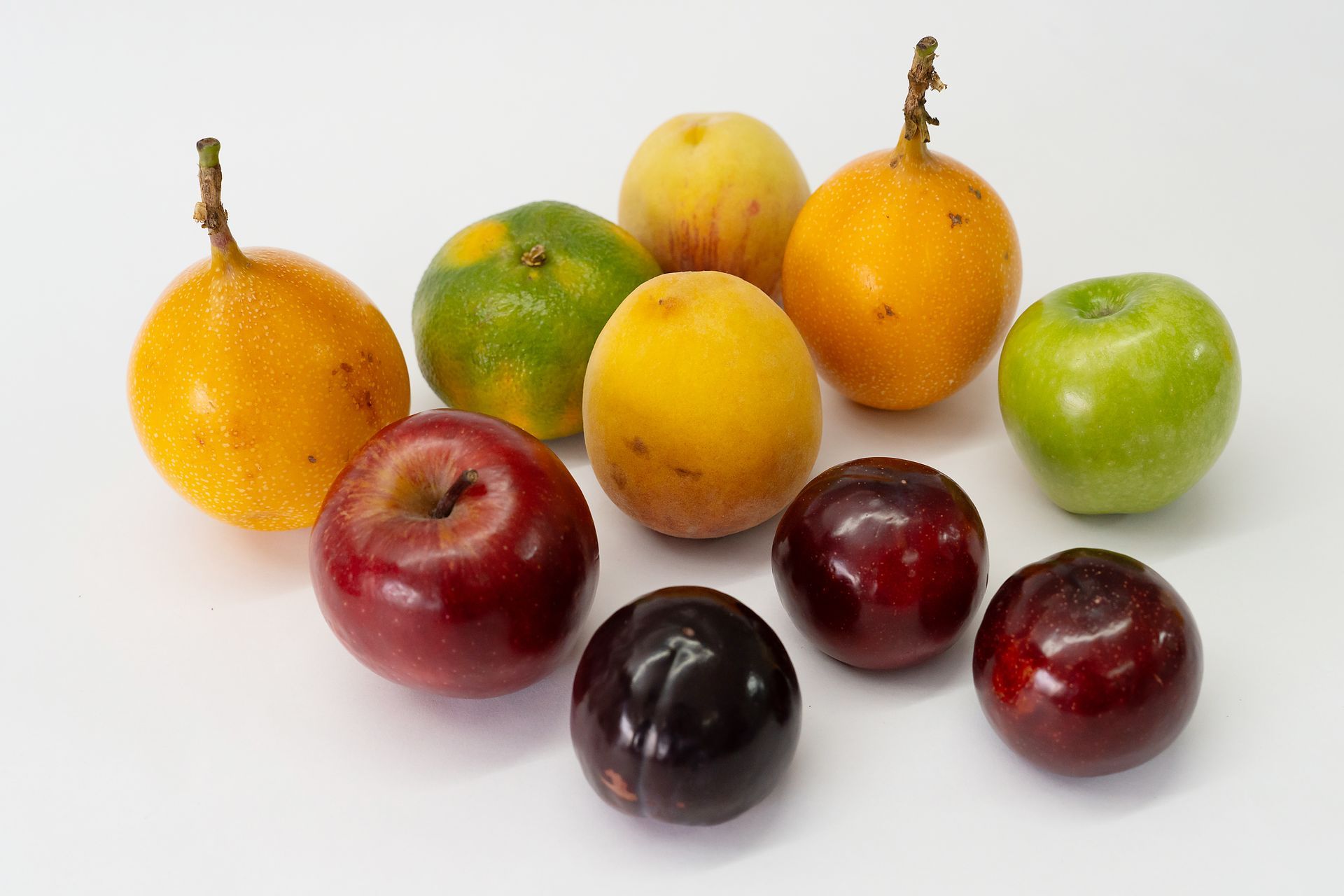 Variedad de frutas maduras y ciruelas dispuestas sobre una superficie blanca.
