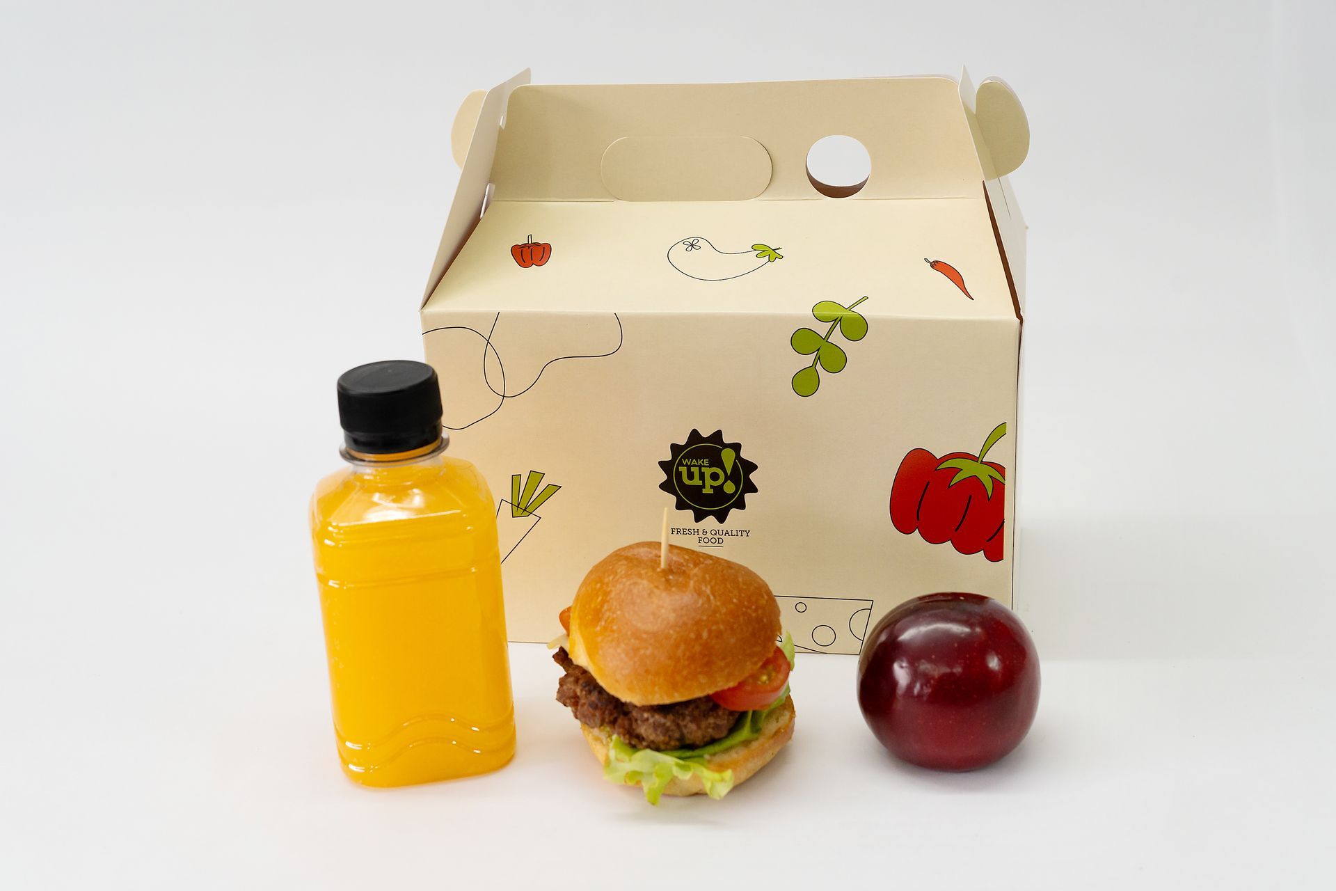 Comida para llevar con hamburguesa, bebida amarilla y manzana roja frente a una caja de marca.