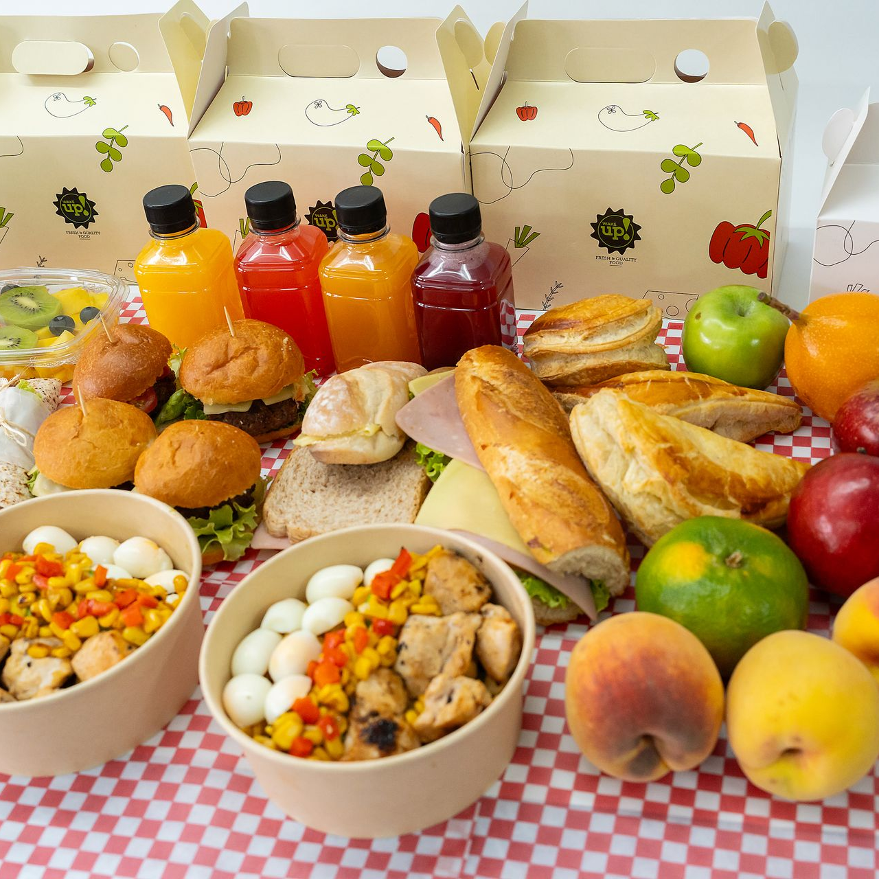 Variedad de pasteles, frutas y bebidas embotelladas dispuestas sobre una mesa a cuadros con cajas de panadería 