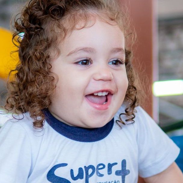 uma garotinha de cabelos cacheados está vestindo uma camisa branca com a palavra super+