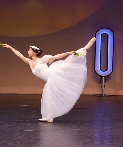 Ballet dancer in a white dress holds an arabesque on stage.
